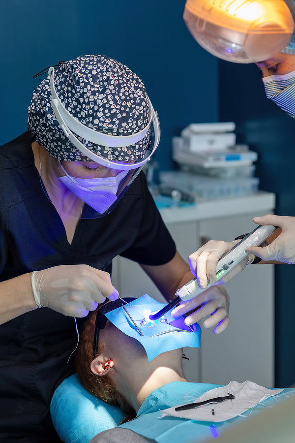 Dentist and assistant using dental curing light on patient’s tooth. Concept of adhesive dentistry, cavity filling, and modern cosmetic dental treatment.