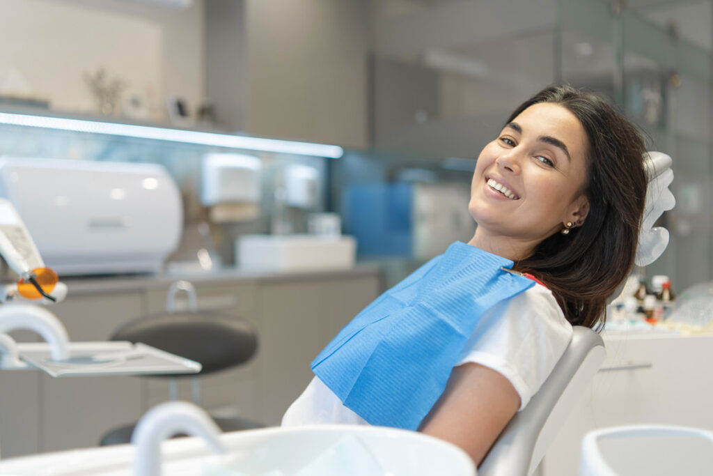 Pretty brunette happy female patient sitting in the chair at dental clinic