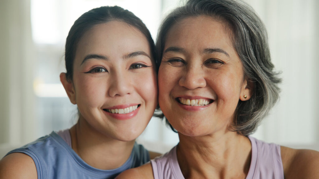 May Mother's day young adult child smile look at camera cuddle hug mature middle age old mum. Love kiss care mom asia elder aged people sit at home sofa happy enjoy family good time aging life.