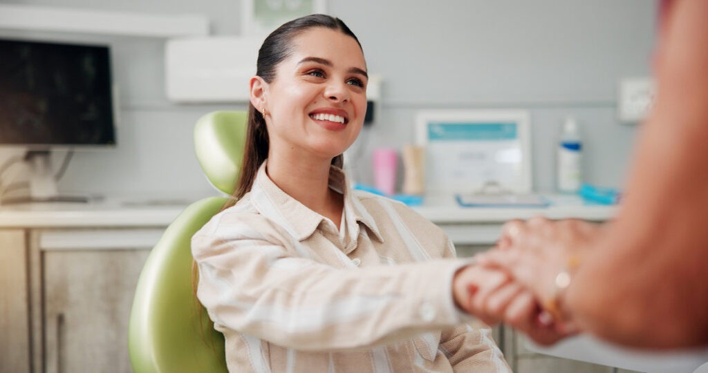 Woman, holding hands and smile at dentist for oral hygiene, teeth whitening or healthcare checkup. Dental care, patient and support for cavity extraction, root canal service and help or advice.