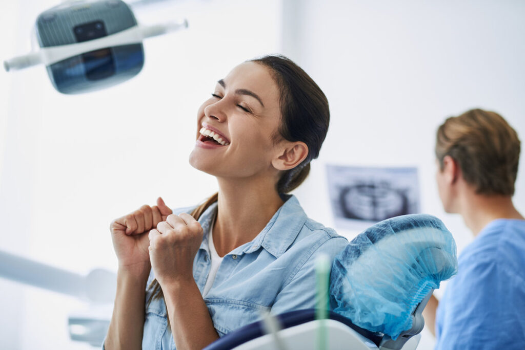 Good news. Portrait of charming woman with closed eyes clenching fists and laughing. Stomatologist with dental xray on blurred background