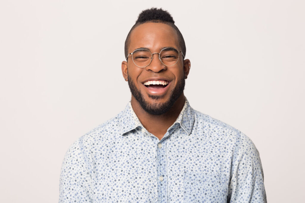 Head shot portrait of cheerful laughing young African American man in glasses isolated on studio background copy space, funny guy with wide beaming healthy smile looking at camera, feeling happy