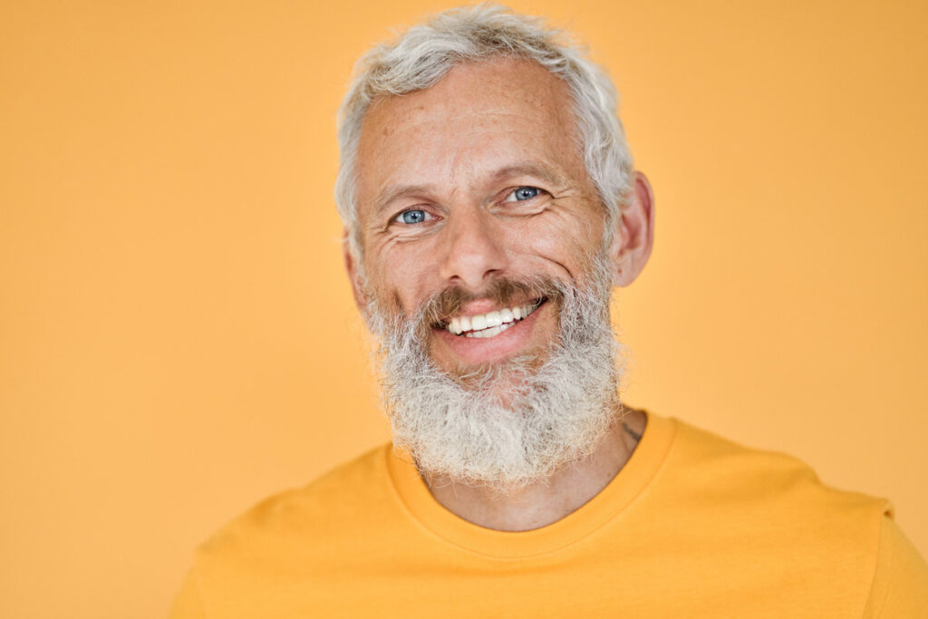 Happy mature older bearded man, smiling cool middle aged gray haired old senior confident hipster wearing yellow t-shirt standing isolated on yellow background, close up headshot portrait.