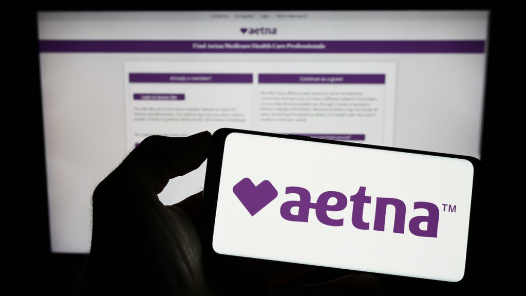 Stuttgart, Germany - 01-14-2023: Person holding mobile phone with logo of American managed healthcare company Aetna Inc. on screen in front of web page. Focus on phone display.
