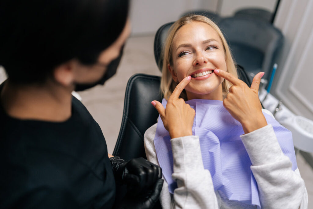 Close-up top view of happy young woman patient pointing with fingers at healthy smile, demonstrating whitening teeth procedure result, satisfied with dental clinic service. Concept of dental treatment